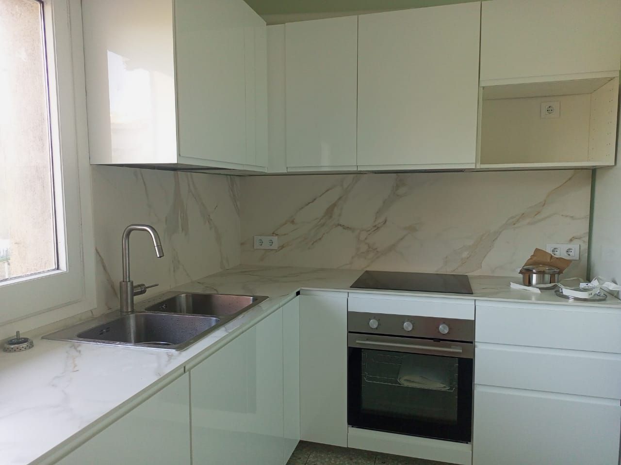 Cocina moderna con armarios blancos, horno integrado, fregadero y encimera de color claro