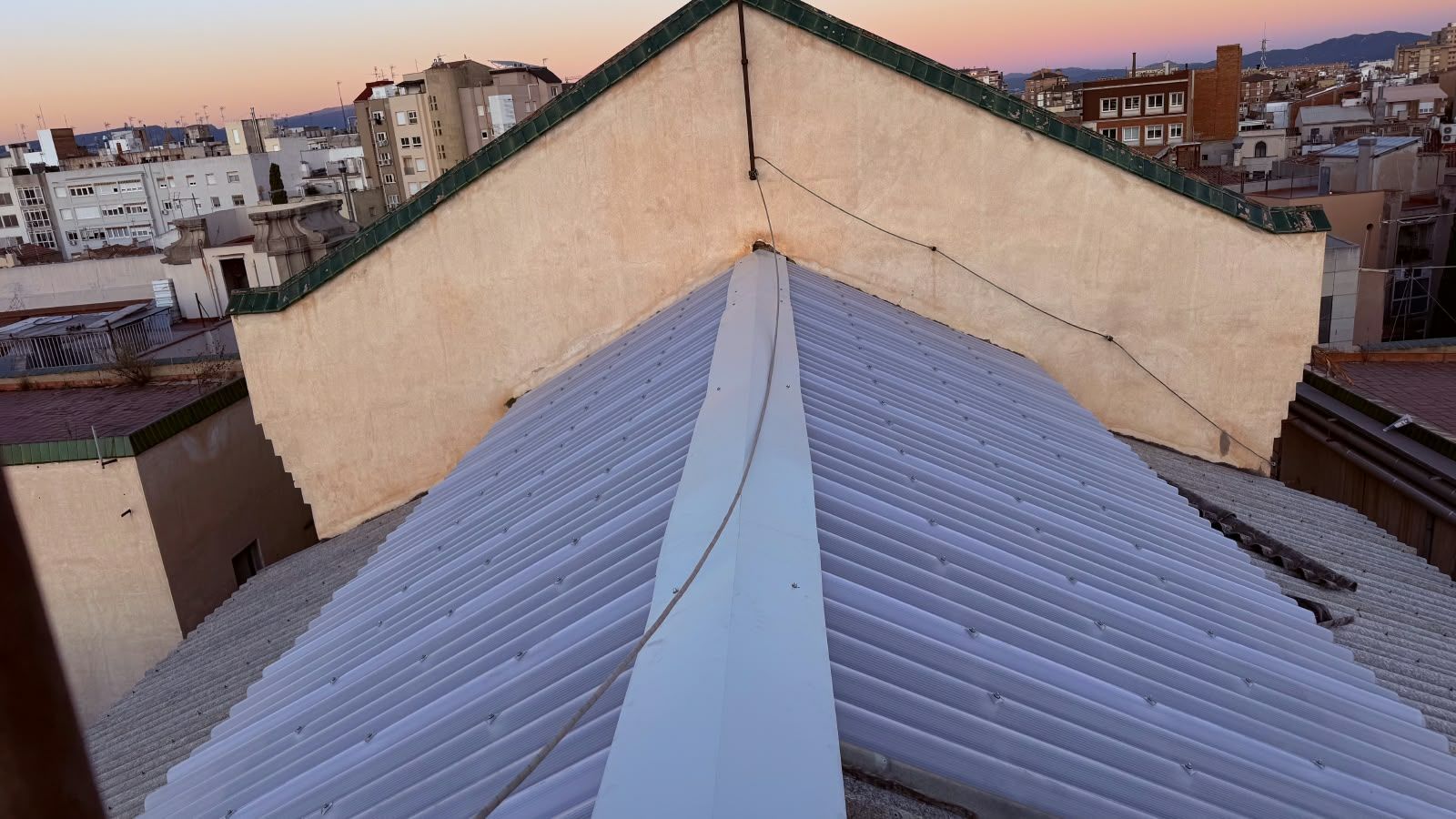 Vista desde una azotea al atardecer, con un tejado metálico que conduce a un horizonte urbano.