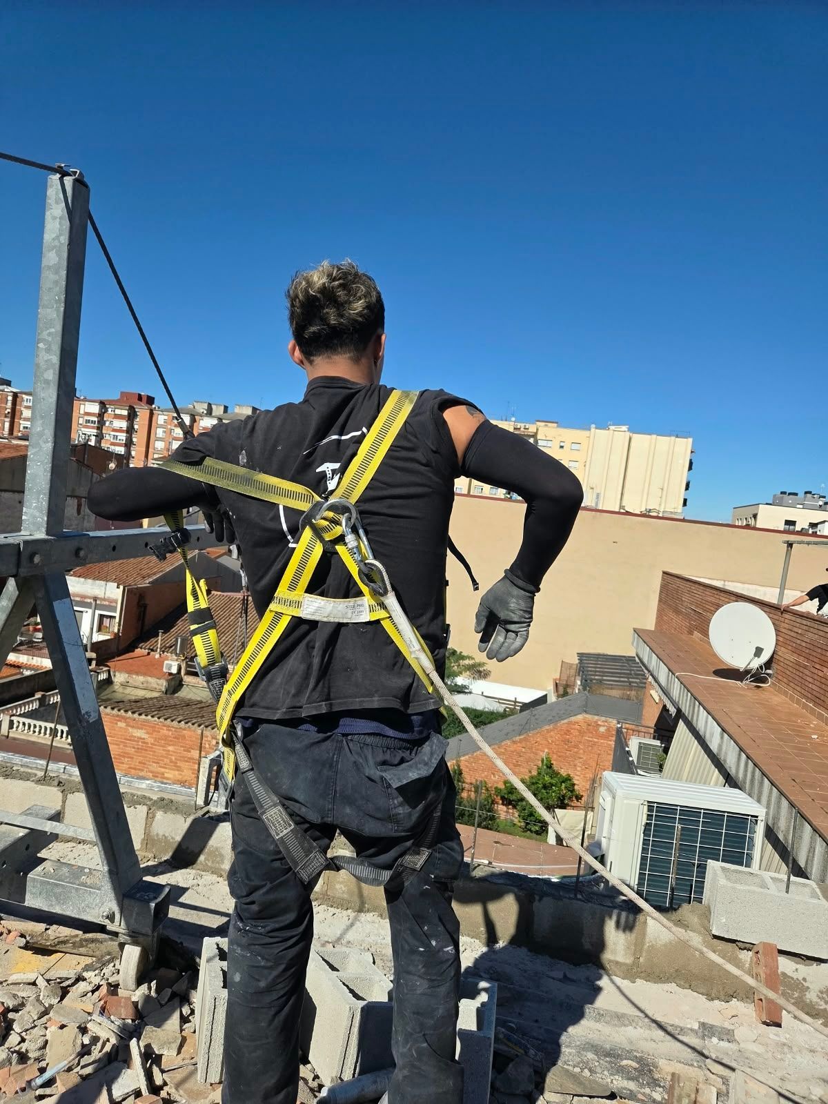 Un trabajador con arnés de seguridad en un tejado en construcción, de espaldas a la cámara.