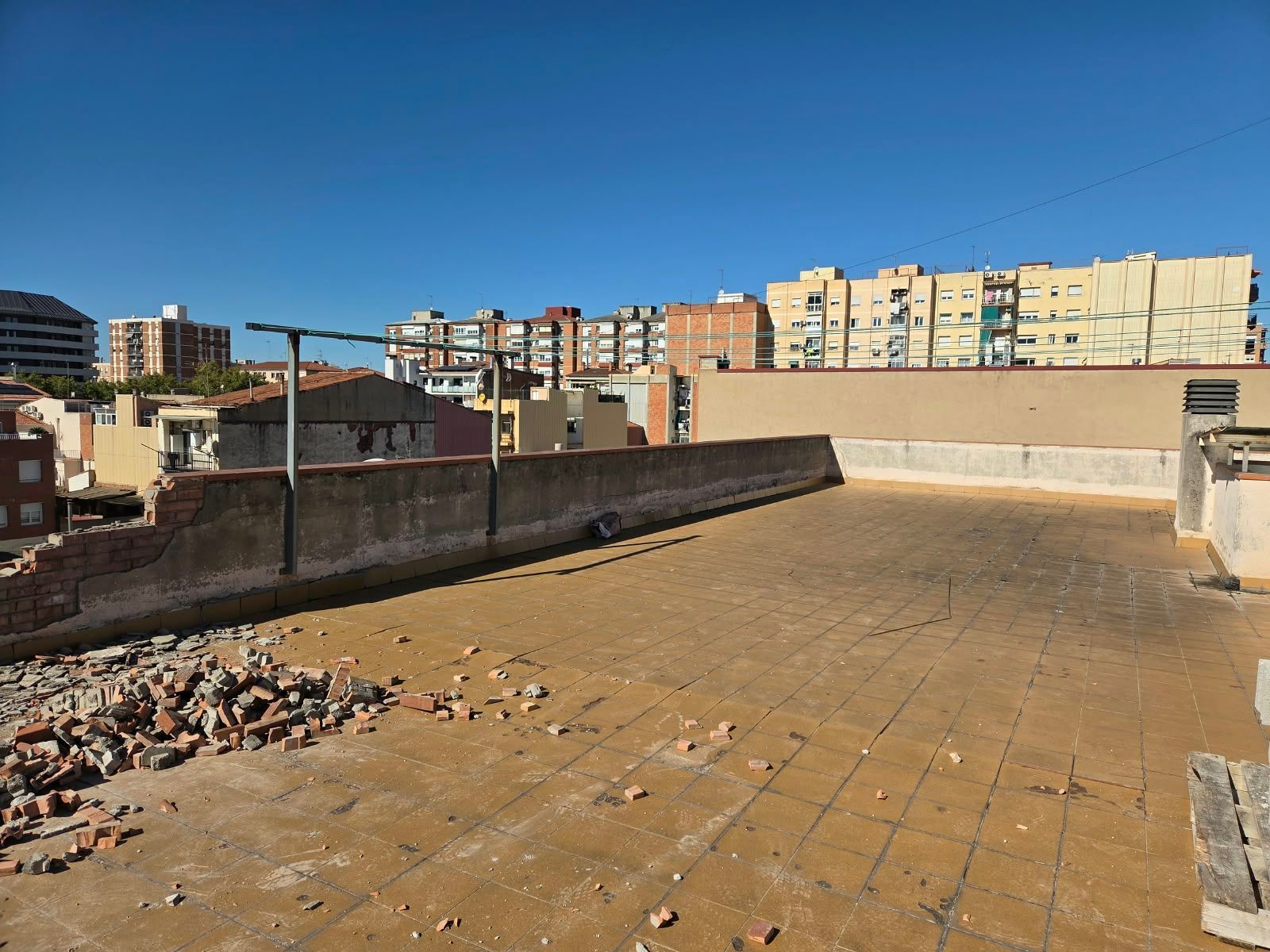 Terraza en la azotea con escombros en primer plano y edificios de la ciudad bajo un cielo azul despejado