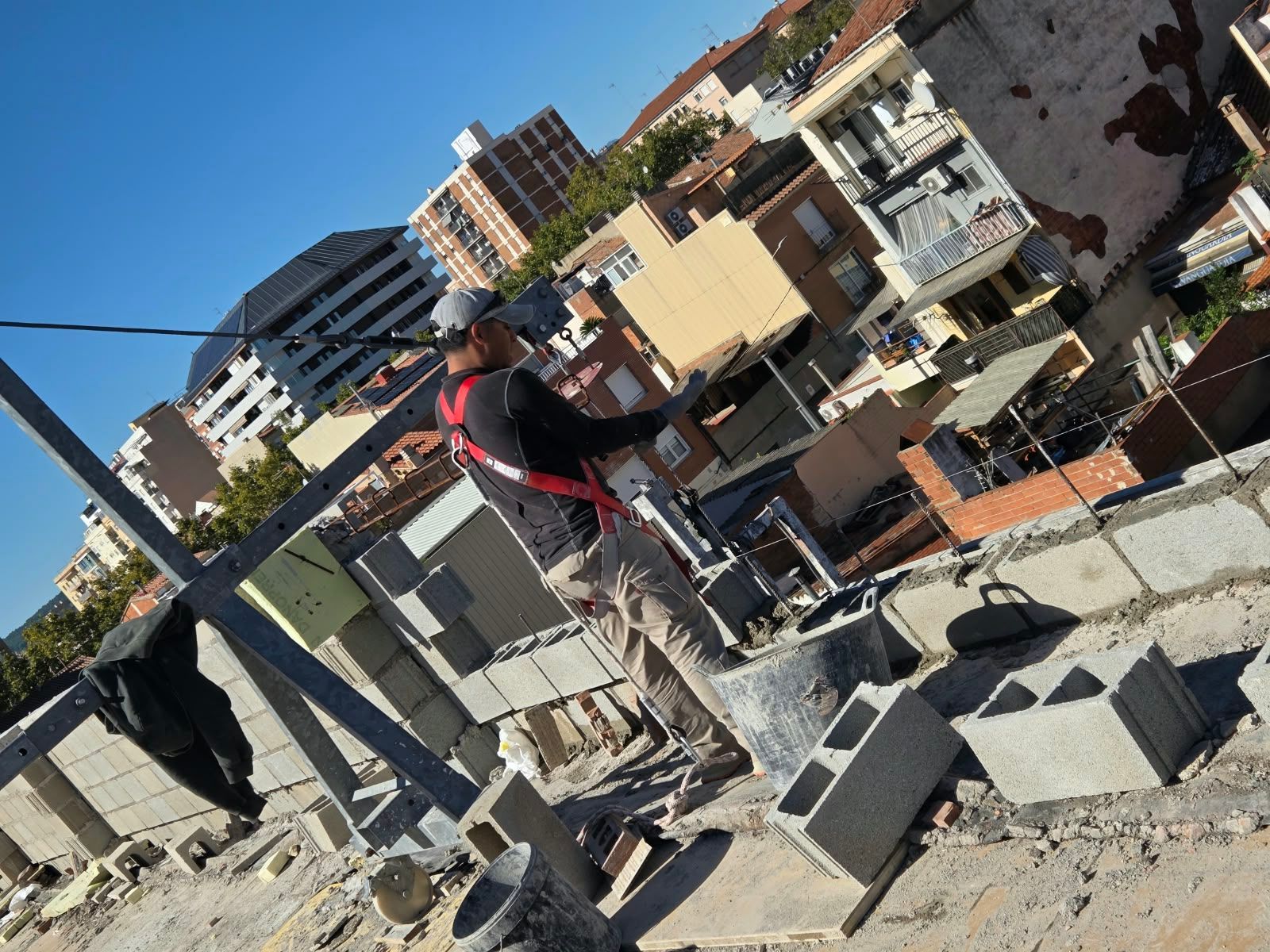 Obrero en una azotea en construcción, con bloques de hormigón y escombros, y edificios de la ciudad al fondo.