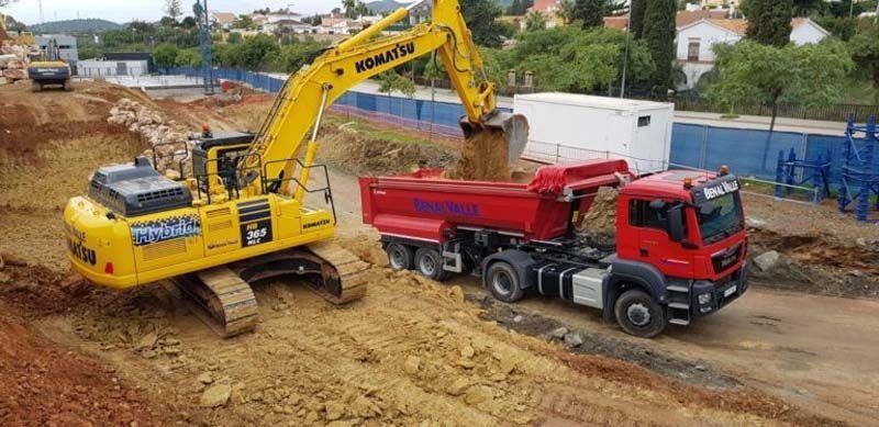 Una excavadora amarilla está cargando tierra en un camión volquete rojo.