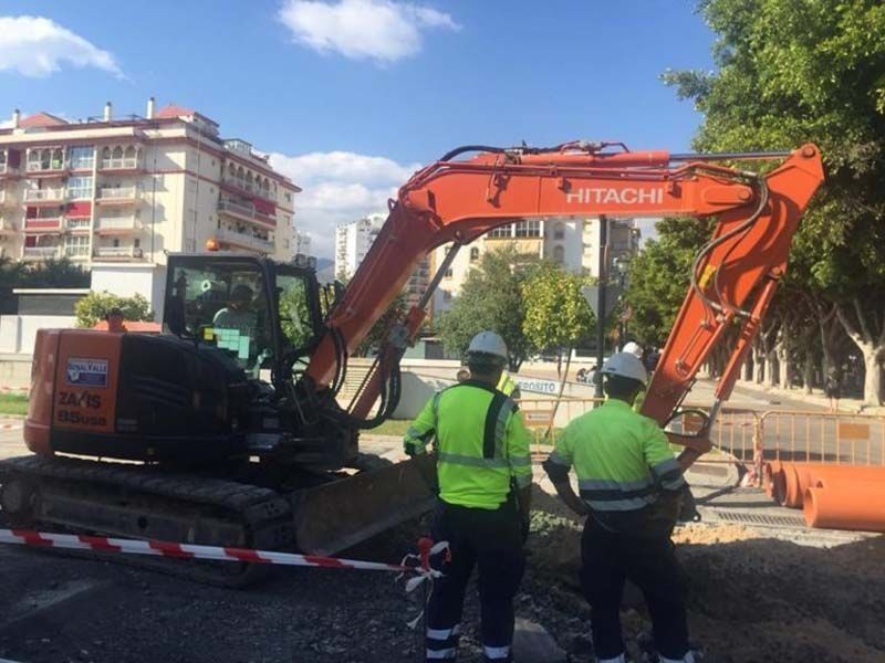Un grupo de trabajadores de la construcción está parado frente a una excavadora Hitachi.