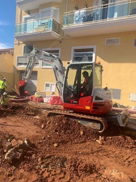 Una excavadora roja y blanca está parada en el suelo frente a un edificio.