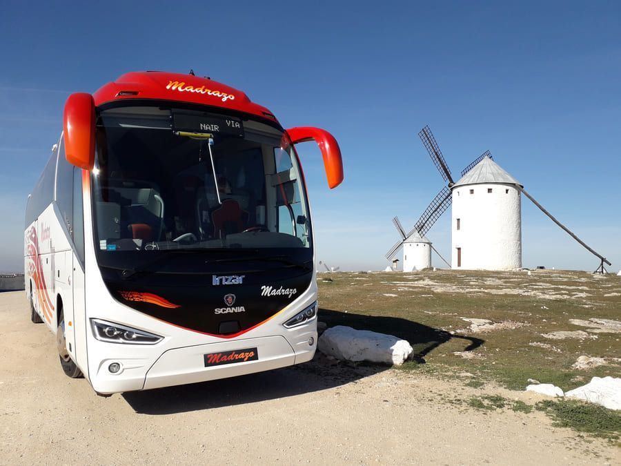 Un autobús rojo y blanco está estacionado frente a un molino de viento.
