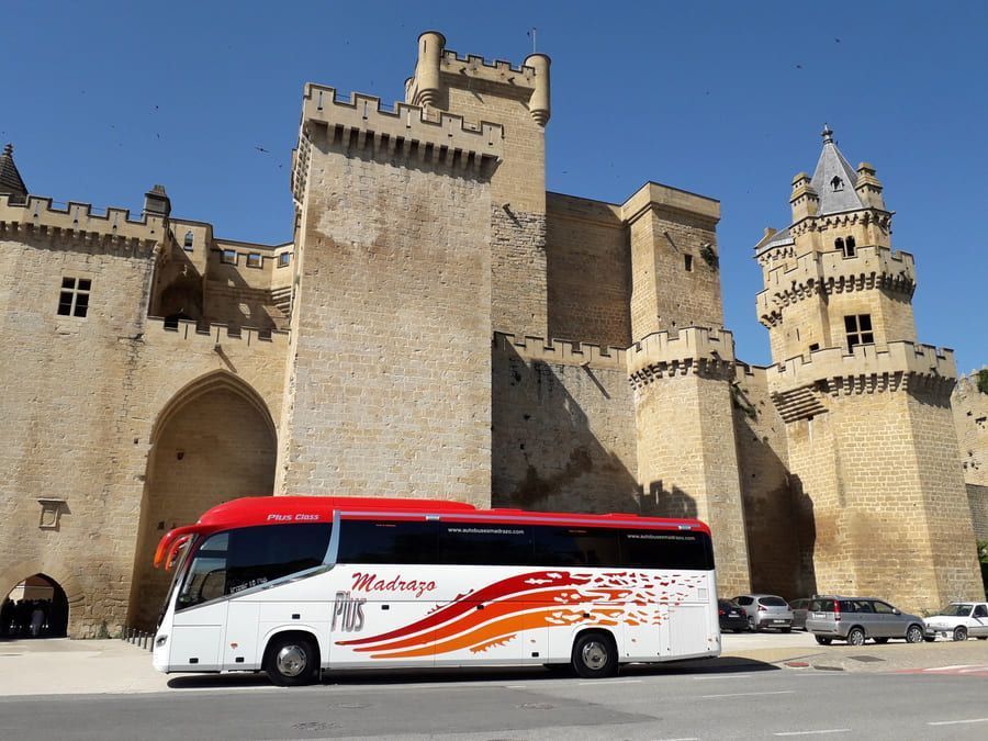 Un autobús rojo y blanco está estacionado frente a un castillo.