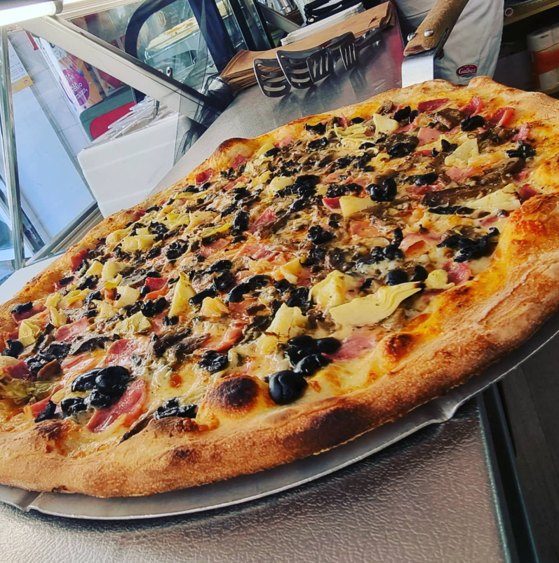 Pizza grande con olive, formaggio e condimenti su un vassoio in un ristorante informale.