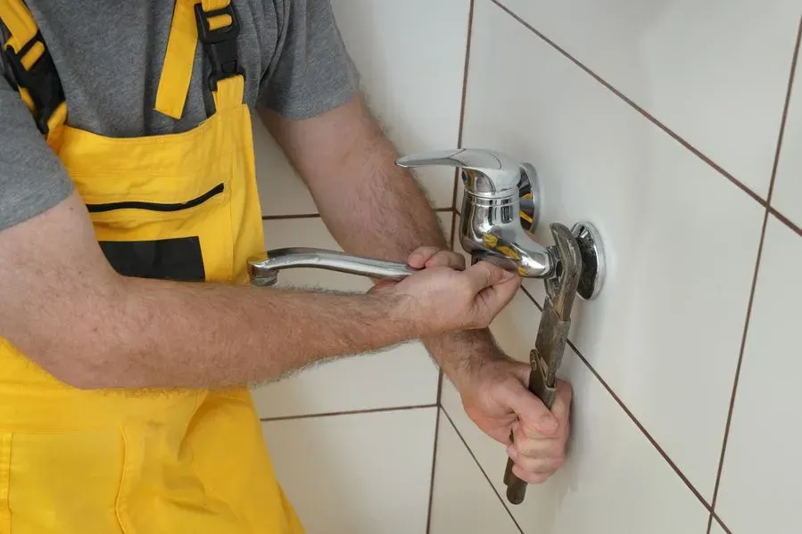 Un hombre está arreglando un grifo en un baño con una llave inglesa.