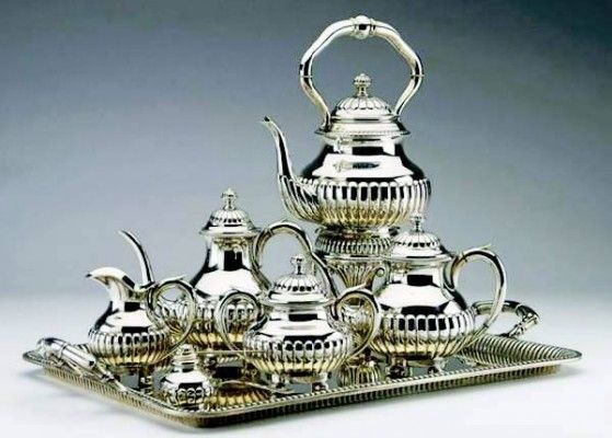 Un juego de té de plata está sobre una bandeja de plata.