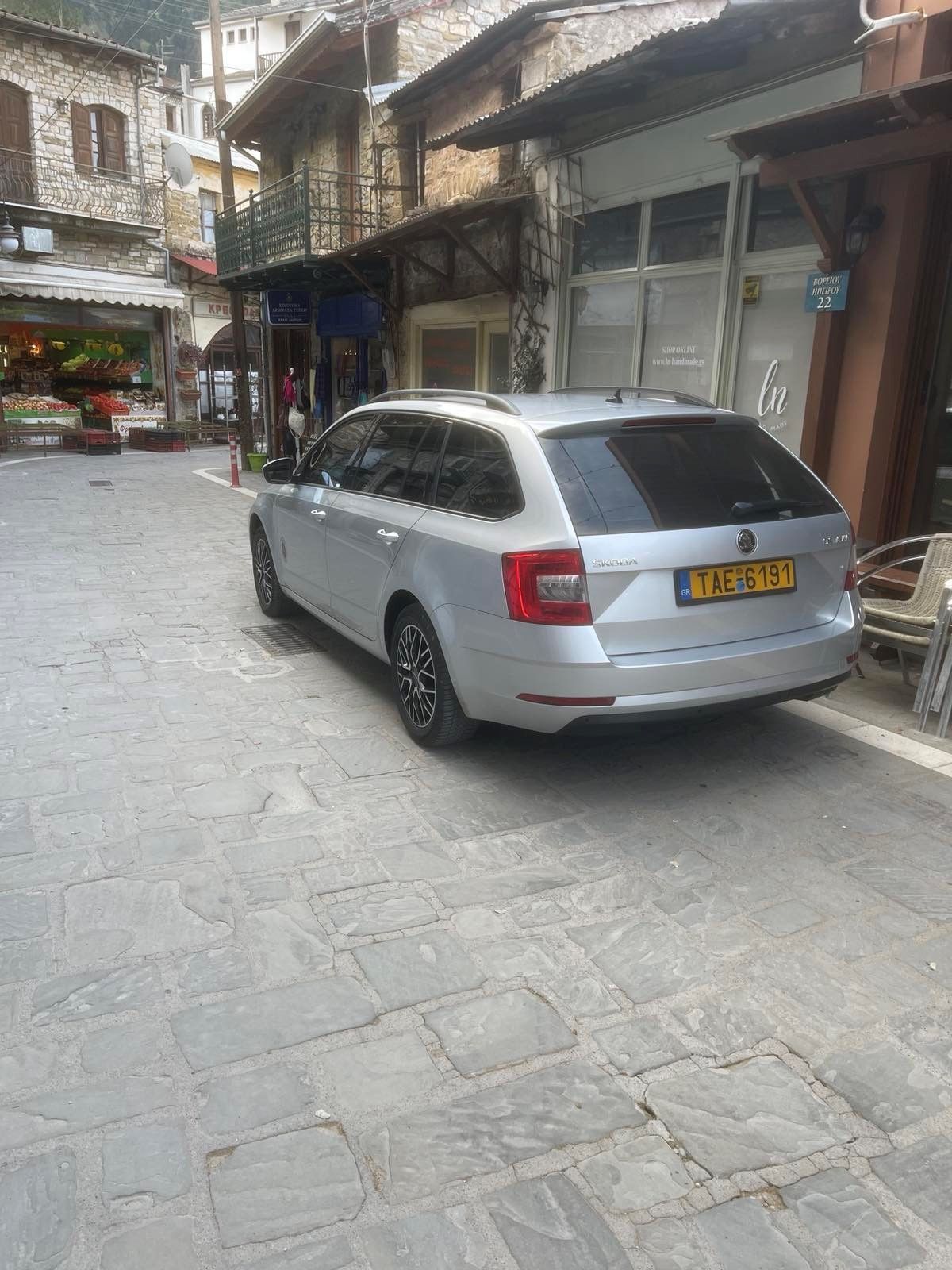 Ασημένιο SUV παρκαρισμένο σε έναν στενό πλακόστρωτο δρόμο ανάμεσα σε παλιά κτίρια και βιτρίνες καταστημάτων.