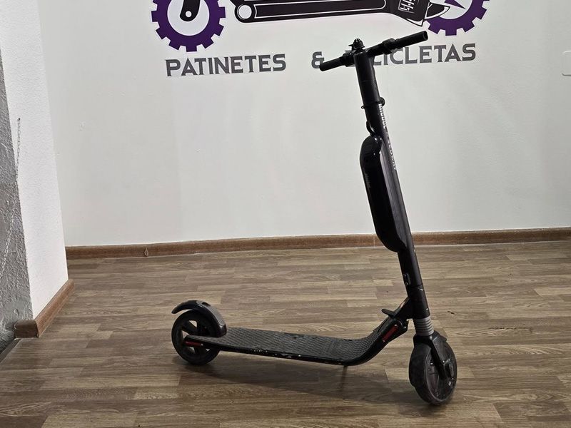 Un scooter negro está sentado en un piso de madera frente a una pared que dice patinetes y bicicletas