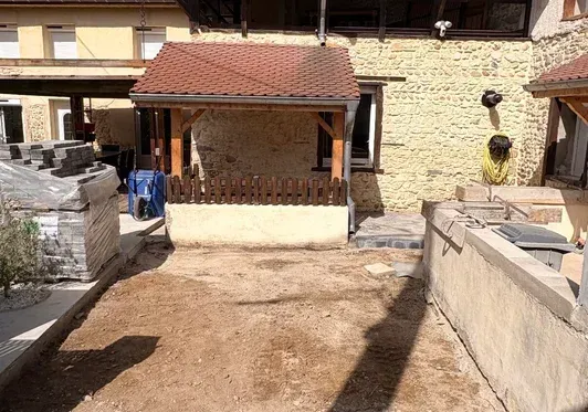 Cour intérieure avec un petit porche, des murs en pierre et un chemin de terre au premier plan.