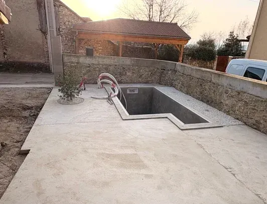 Terrasse en béton avec piscine ou spa rectangulaire encastré, murs en pierre et maison en arrière-plan