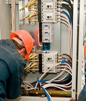 Un hombre que lleva un casco está trabajando en una caja eléctrica.