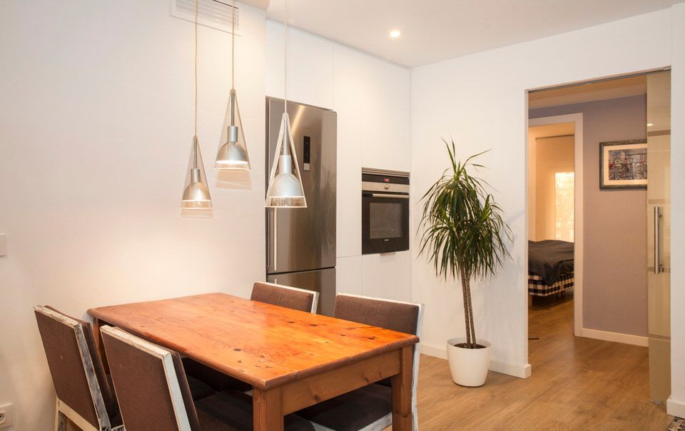 Comedor con una mesa de madera preparada para comer, un mueble de madera lleno de platos y una ventana soleada.
