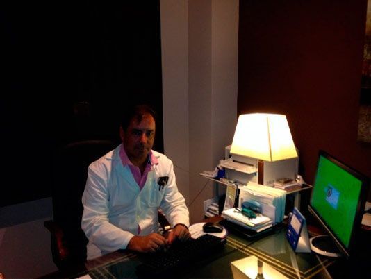 Un hombre con bata de laboratorio se sienta en un escritorio frente a una computadora.