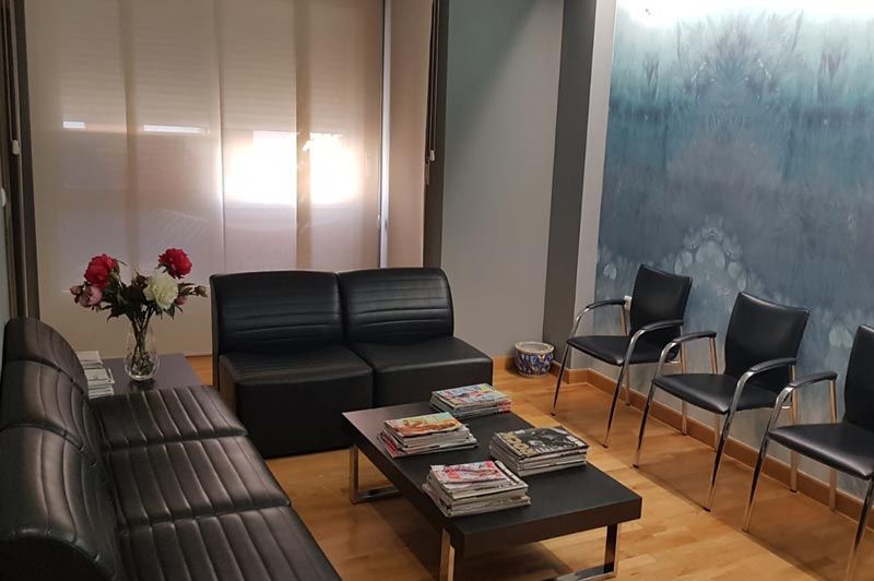 Una sala de espera con un sofá, sillas, una mesa y un jarrón de flores.