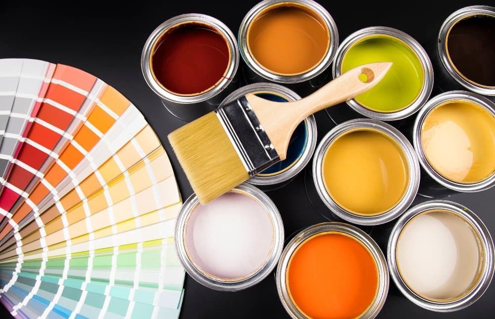 Muestras de pintura y latas de pintura abiertas con un pincel, mostrando opciones de colores brillantes.