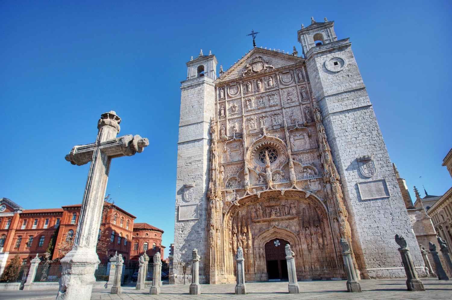 Catedral histórica de piedra con fachada ornamentada y gran cruz en una plaza soleada bajo un cielo azul.
