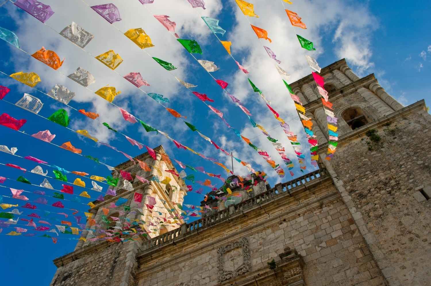 Banderas de oración coloridas colgadas sobre la torre de piedra de una iglesia contra un cielo azul