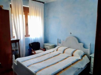Habitación luminosa con paredes azules, cortinas blancas y una cama sin hacer con ropa de cama a rayas.