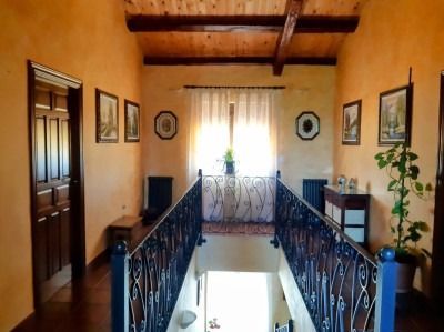 Pasillo con barandilla de balcón de hierro forjado, paredes naranjas, vigas de madera en el techo y cuadros enmarcados junto a una ventana luminosa.