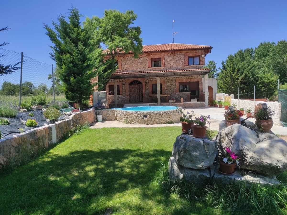 Casa de piedra con piscina, césped verde y jardín bajo un cielo azul despejado.