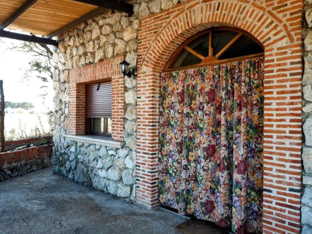 Patio de piedra y ladrillo con puerta arqueada cubierta por una cortina colorida.