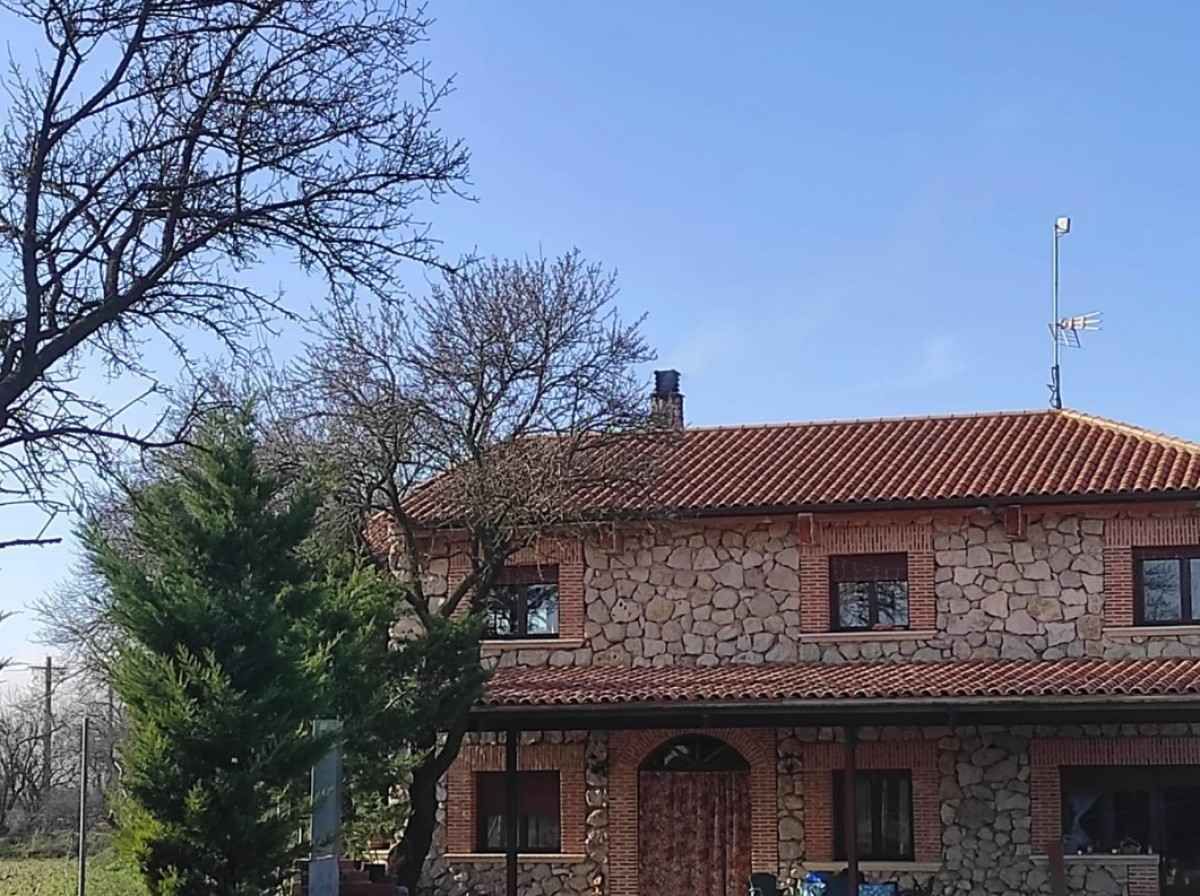 Casa de piedra con tejado de tejas rojas y árboles desnudos bajo un cielo azul despejado.