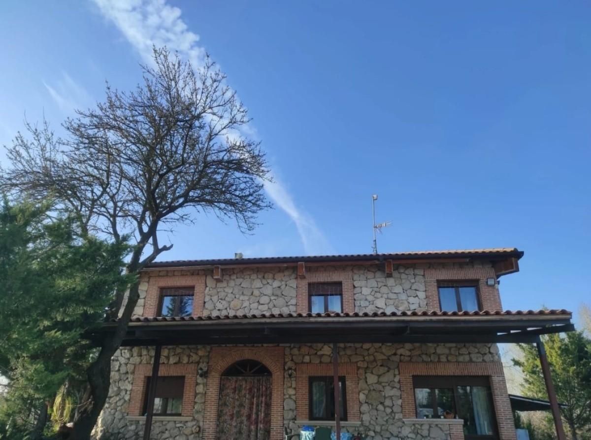 Casa de piedra con tejado de tejas rojas y un árbol sin hojas contra un cielo azul.