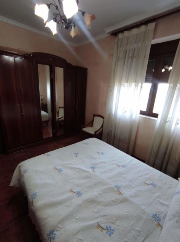 Dormitorio con cama, armario de madera oscura, ventana con cortinas, ventilador de techo y luces.