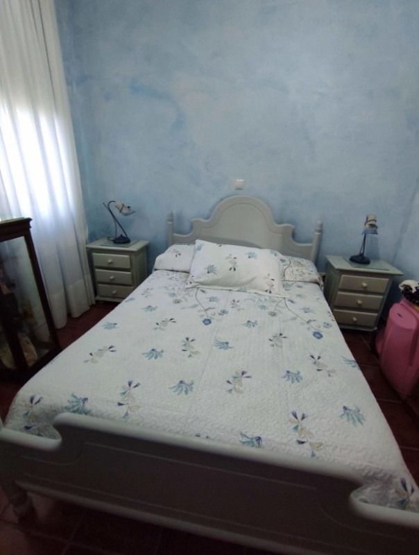 Habitación pequeña con cama blanca, paredes azul claro y mesitas de noche a juego.