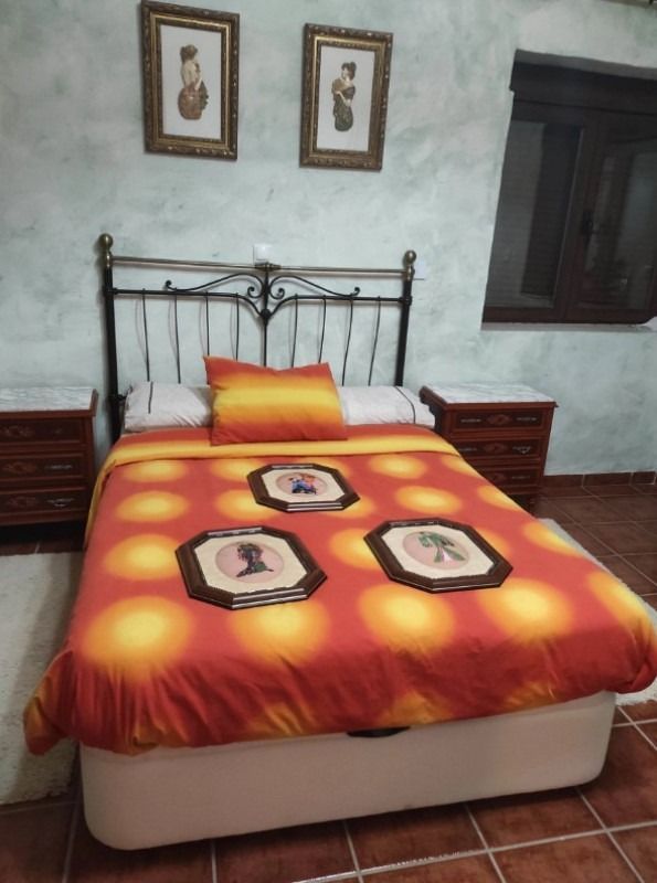Dormitorio con cama de hierro forjado, colcha con estampado naranja, mesitas de noche de madera y cuadros enmarcados en la pared.