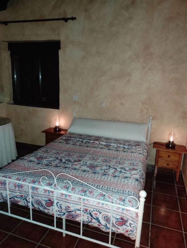 Dormitorio con cama de metal blanco, colcha estampada, lámparas de noche y suelo de baldosas de terracota.