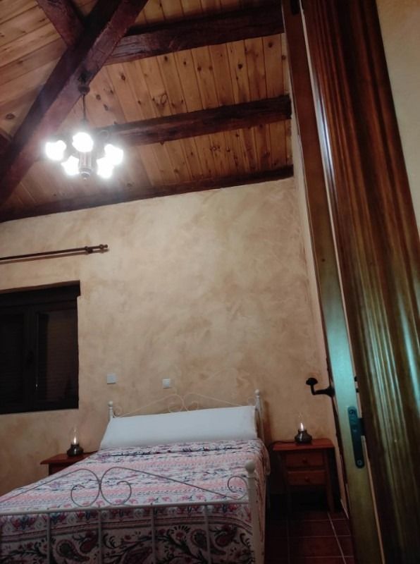 Dormitorio rústico con vigas de madera en el techo, cama, mesitas de noche y lámpara de araña.