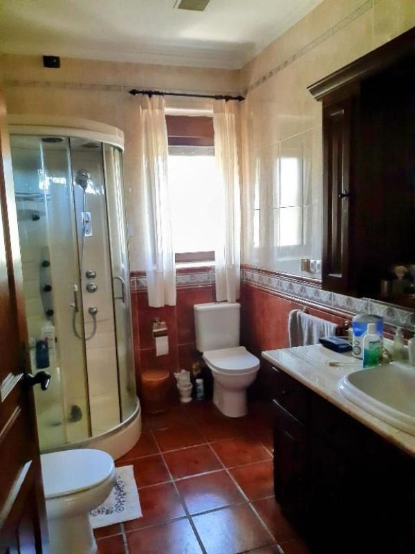 Baño con cabina de ducha, inodoro, lavabo y suelo de baldosas de terracota, iluminado por una ventana.