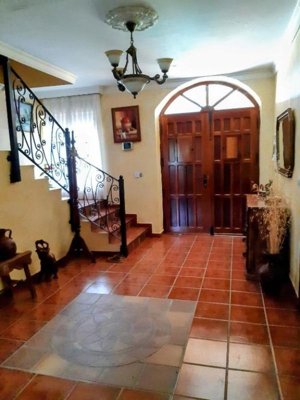 Vestíbulo interior con suelo de baldosas rojas, escalera y puertas dobles de madera.