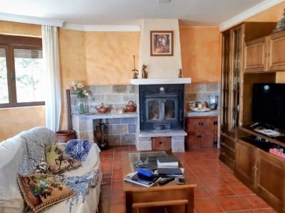 Acogedora sala de estar con paredes color beige, suelo de baldosas, chimenea, sillón, televisor y armarios de madera.