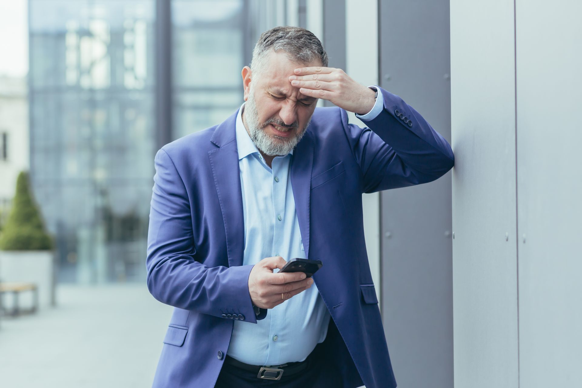 Um homem de fato está encostado na parede enquanto olha para o celular.