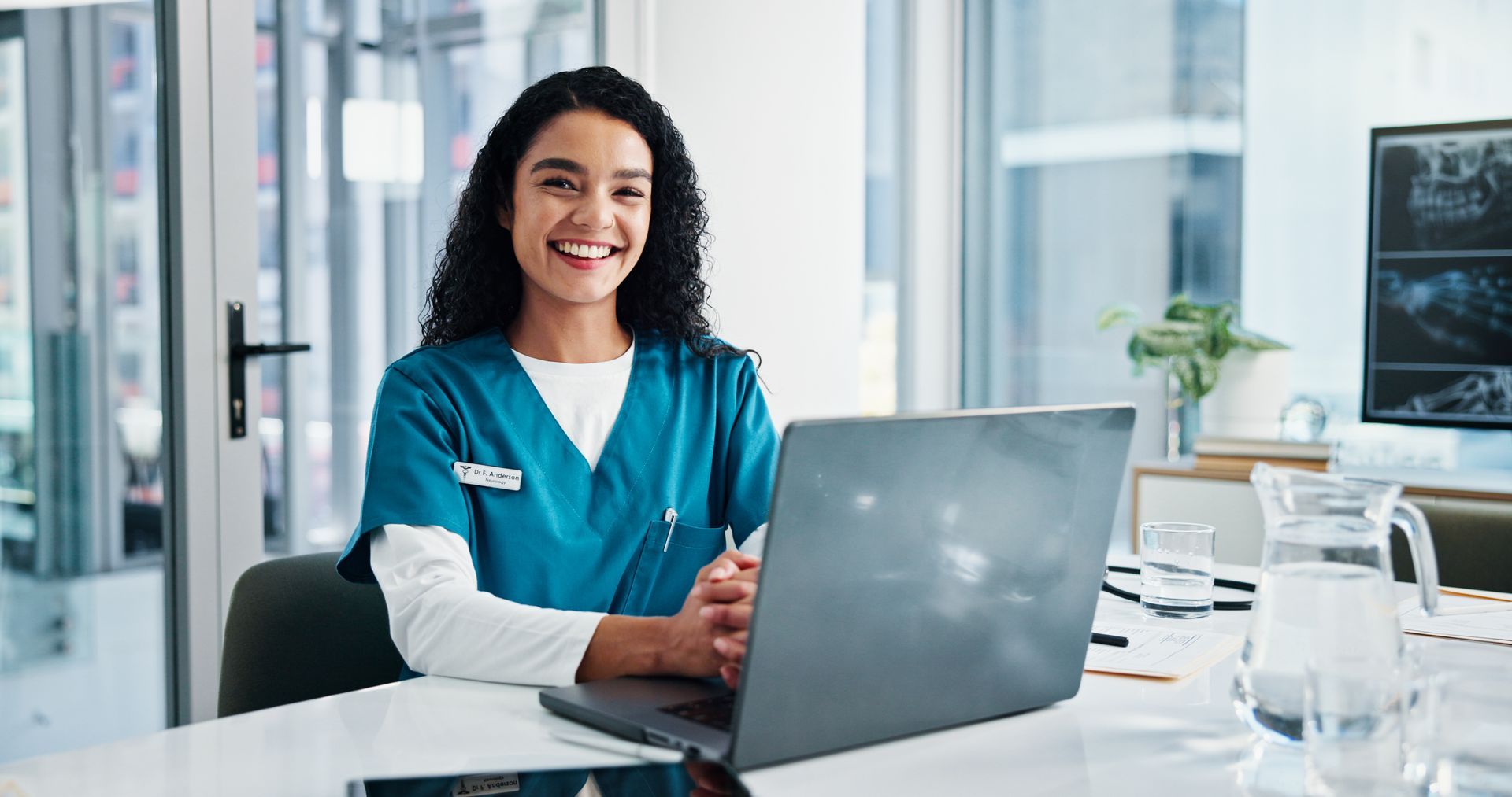 Uma mulher sorridente está sentada em uma mesa em frente a um computador 