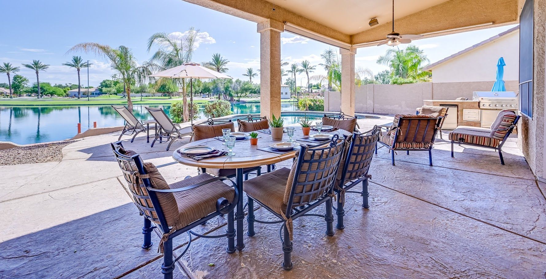 Patio with table, chairs, pool, and lake view under a covered area. Sunny day.