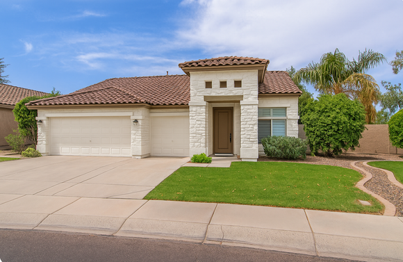 Single-story suburban house with two-car garage, front lawn, and paved driveway under a blue sky