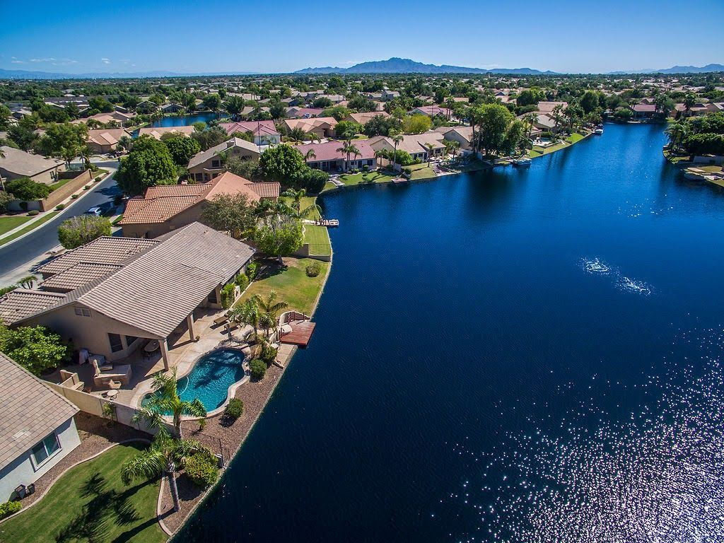 Aerial view of lakeside homes with tiled roofs beside a dark blue water canal under a clear sky.