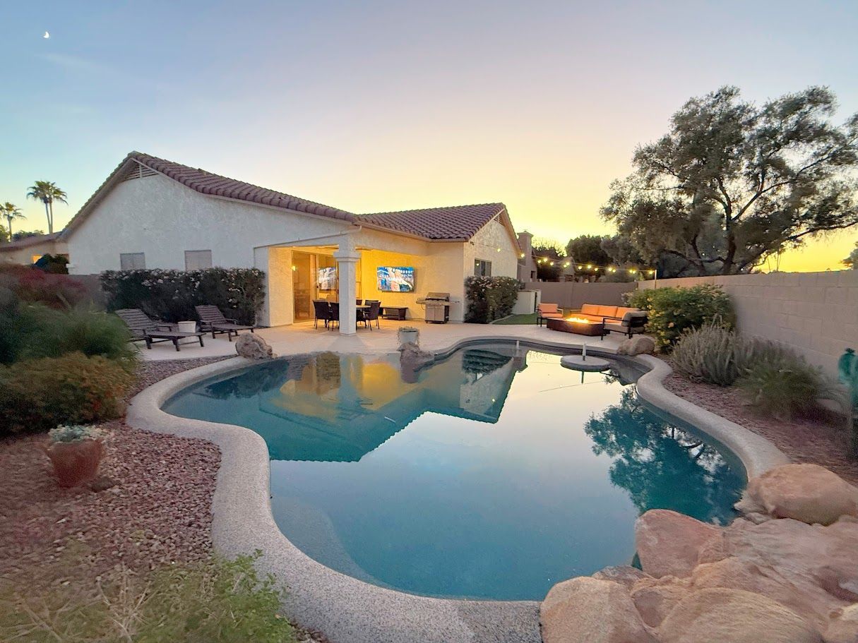 Backyard with pool, patio, and sunset. Turquoise water, tan house, and evening sky.