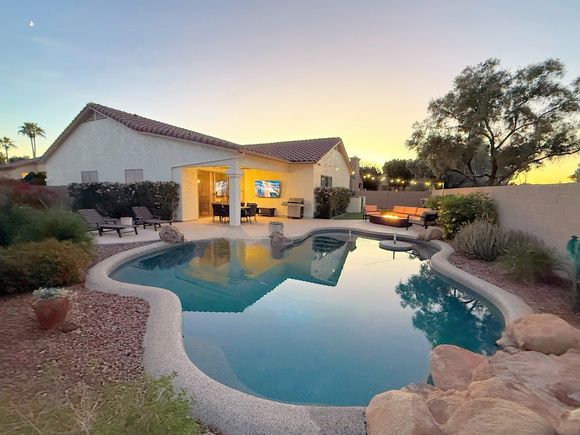 Backyard pool at sunset with a patio, house, and desert landscaping
