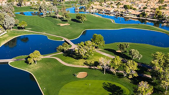 Aerial view of a golf course with green fairways, sand bunkers, and blue water hazards beside homes.