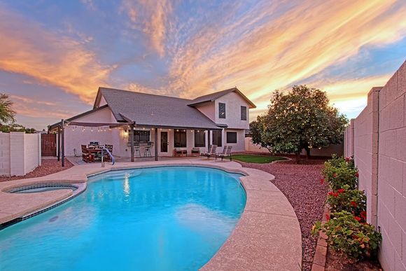 Backyard pool at sunset beside a house, with a curved patio and colorful sky