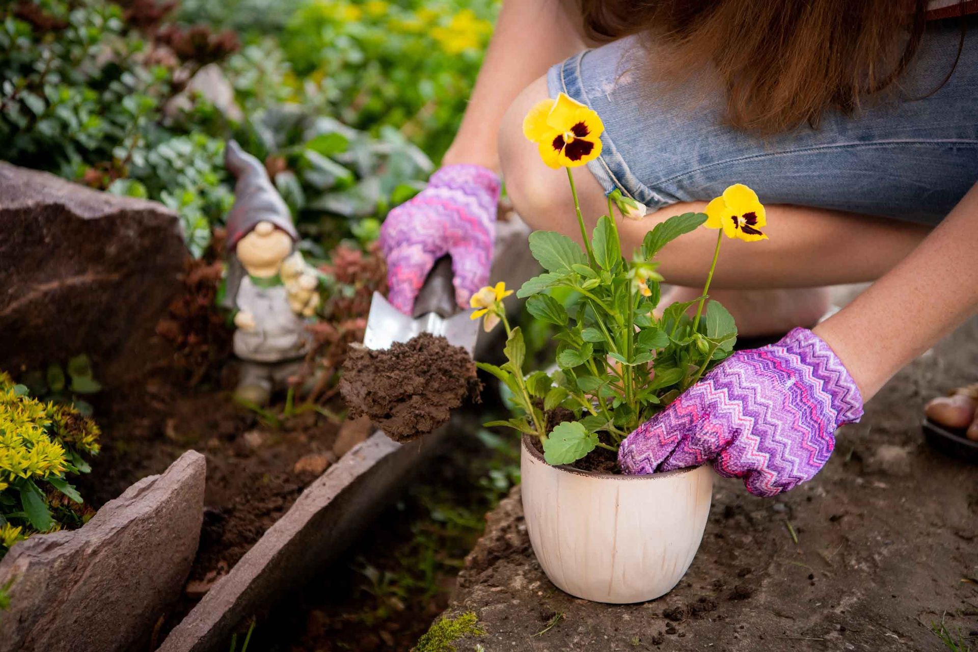 Una mujer está plantando flores en una maceta en un jardín.