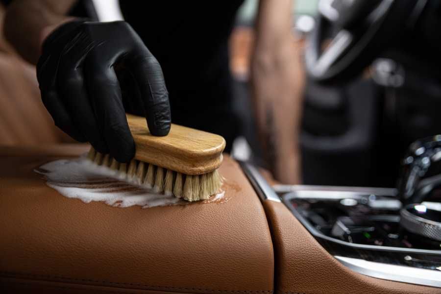 Eine Person reinigt die Lederausstattung eines Autos mit einer Bürste .