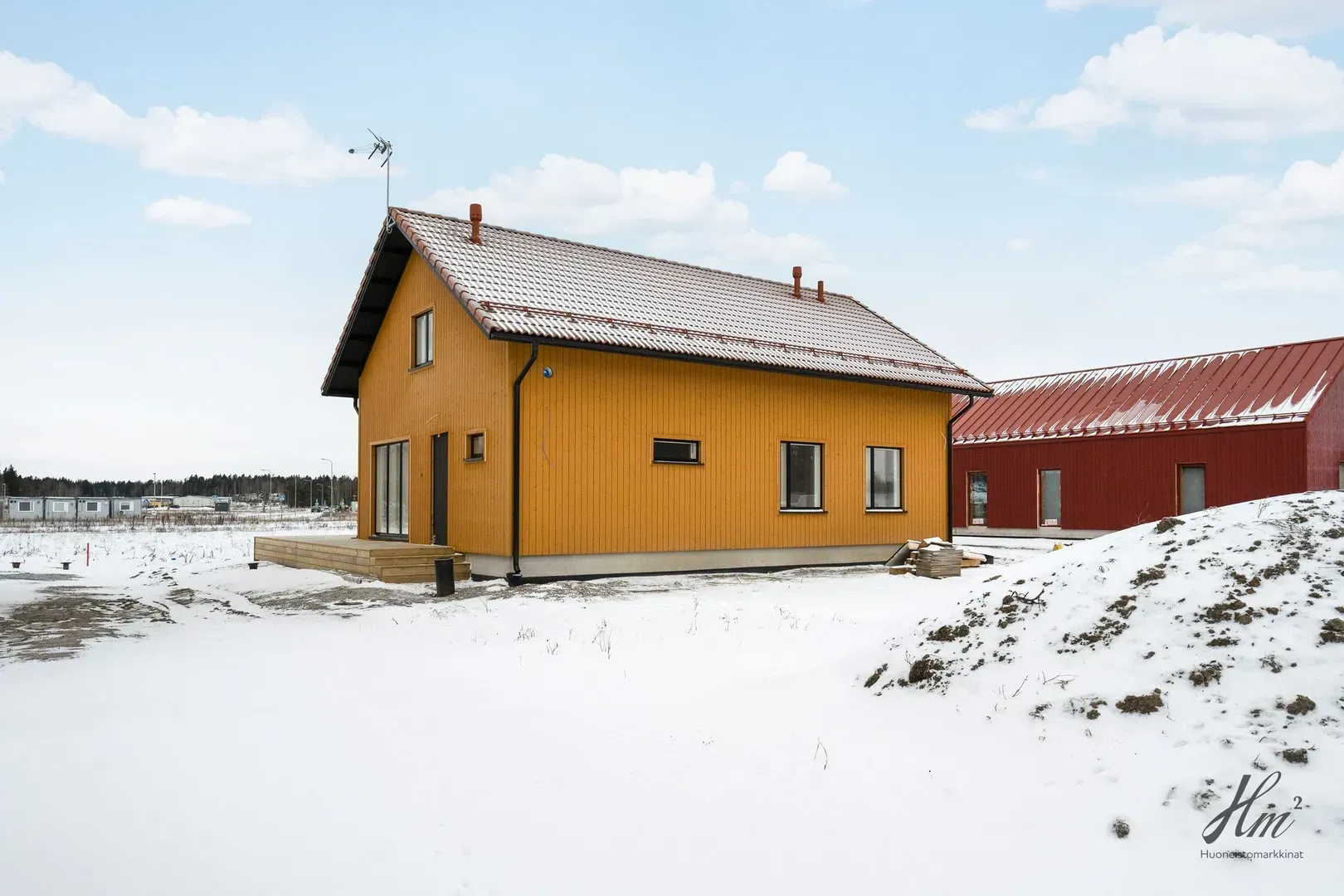 Keltainen talo ja punainen lato lumisessa maaseutumaisemassa osittain pilvisen taivaan alla